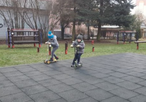 Chłopcy jeżdżą na hulajnogach na boisku przedszkolnym.